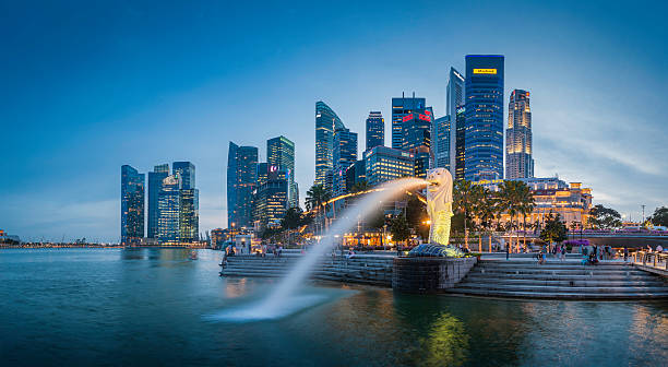 "Singapore, Singapore - 14th February 2012: The crowded cityscape of Central Business District skyscrapers overlooking the Merlion fountain on the Marina Bay waterfront at dusk as tourists and locals enjoy the warm evening promenade, Singapore. Composite panoramic image created from six contemporaneous sequential photographs."